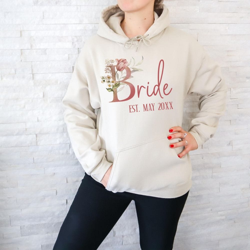 Customizable floral bride hoodie for fiancée, wife, spouse, BFF or bestie on your wedding or anniversary. Great idea for engagement announcement, bachelorette party, bridesmaid proposal box gift idea, rehearsal dinner, and after wedding party. This cute getting ready present is a perfect idea for soon-to-be daughter-in-law, future Mrs. bride or as a honeymoon vacation souvenir. Personalize with date for a special touch.